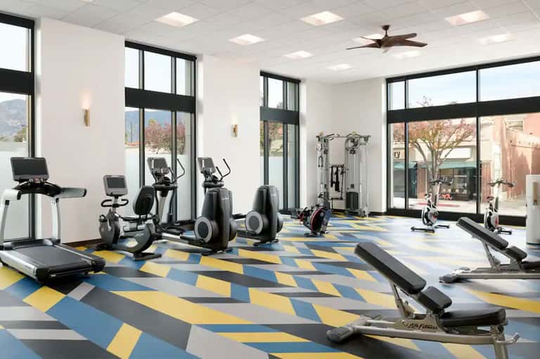 Contemporary fitness center with cardio equipment, windows, geometric flooring, and gym machines