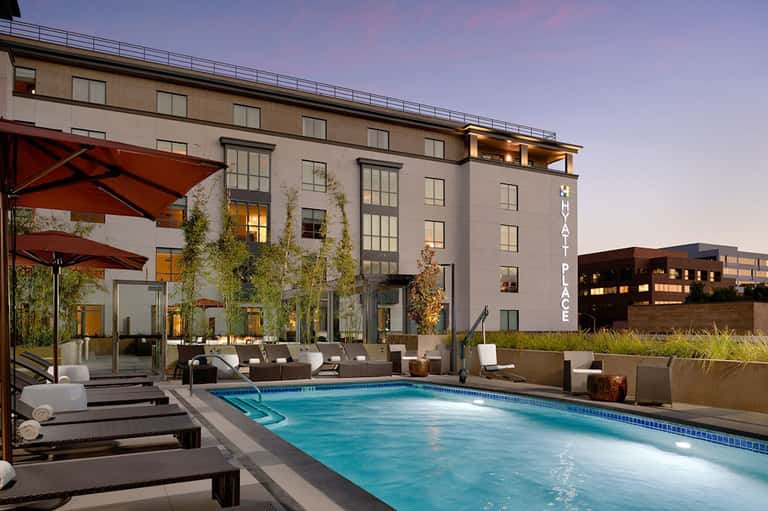 Modern hotel pool deck at dusk with lounge chairs, red umbrellas, and illuminated building