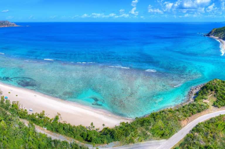 Pristine turquoise cove with white sandy beach, crystal clear water, rocky cliffs, and lush Mediterranean vegetation