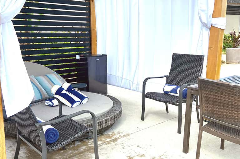 Outdoor lounge area with rattan chairs, striped pillows, sheer white curtains, and wooden privacy screen