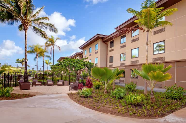 Resort grounds with palm trees, landscaping, seating areas, and multi-story tan-colored hotel building