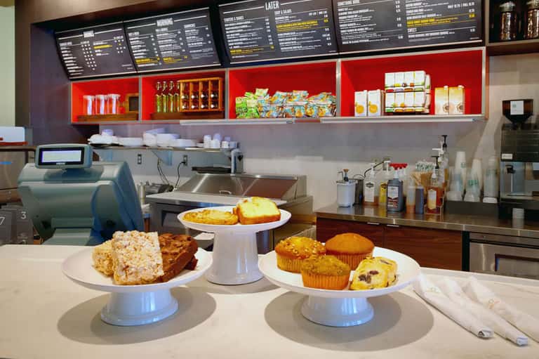 Coffee shop counter with pastries, muffins, and menu boards displayed on shelving