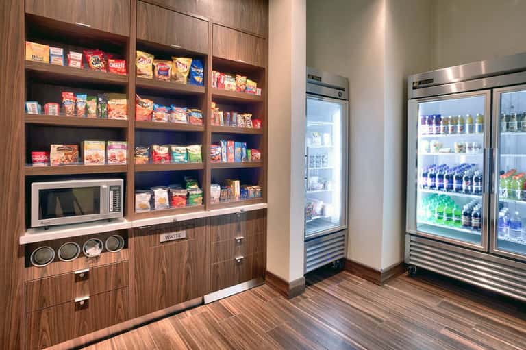 Hotel snack center with wooden shelving, vending machines, and refrigerated beverages