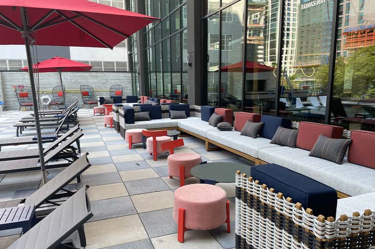 Modern rooftop terrace with red umbrellas, navy and coral seating, and city skyline views