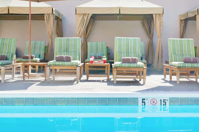 Poolside lounge area with green striped cabanas, white umbrellas, and crystal blue water