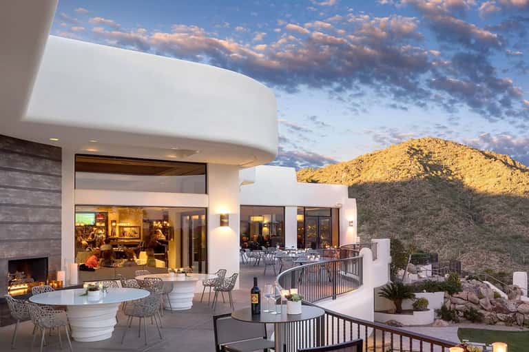 Modern hillside home at dusk with outdoor seating, fireplace, and desert mountain backdrop