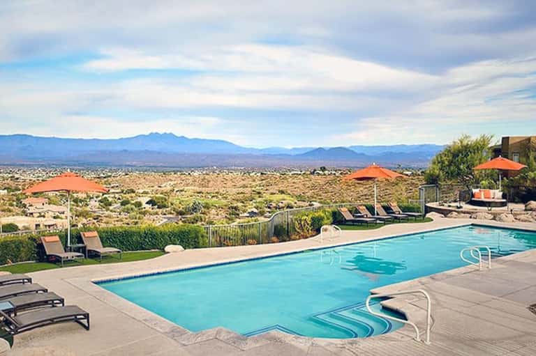 Resort pool with mountain vista, orange umbrellas, lounge chairs, and desert landscape views