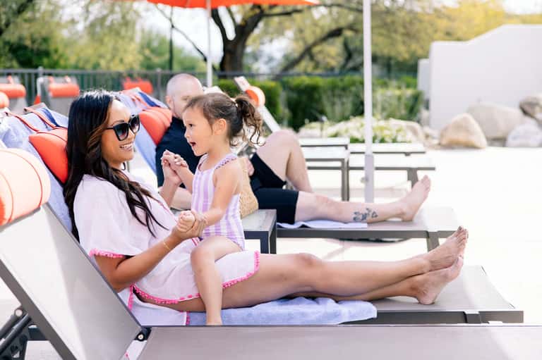 Family relaxing on poolside loungers with colorful umbrellas and landscaped grounds
