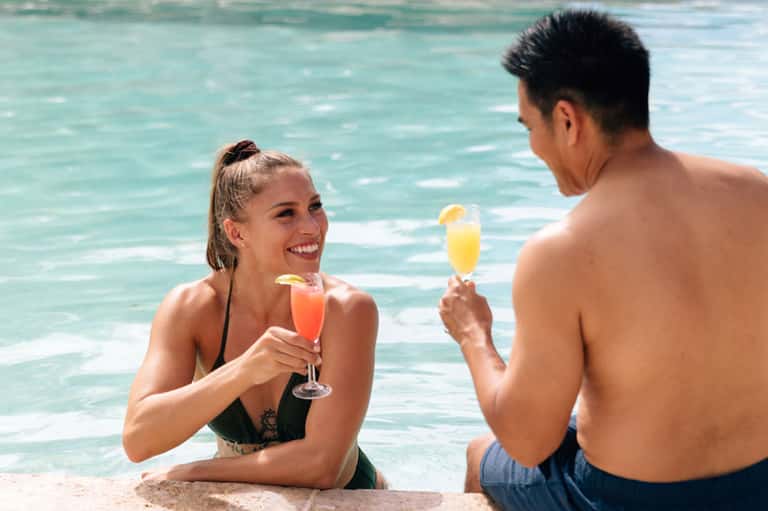 Couple in ocean water toasting with tropical cocktails, smiling together in turquoise Caribbean sea