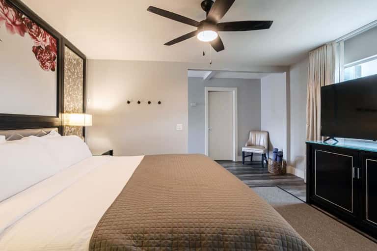 Hotel bedroom with king bed, ceiling fan, and entertainment center
