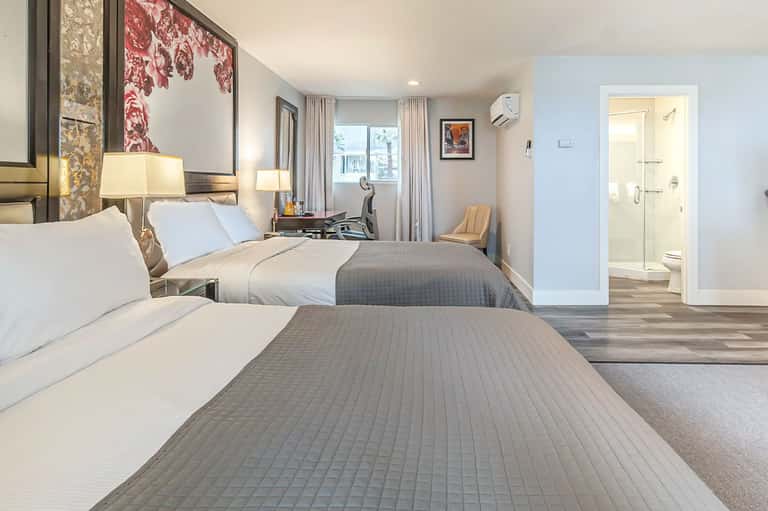 Spacious hotel room with two queen beds, modern furnishings, and ensuite bathroom with ocean view