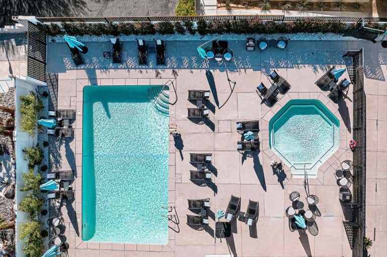 Overhead view of pool deck with turquoise pools, black loungers, and manicured gardens