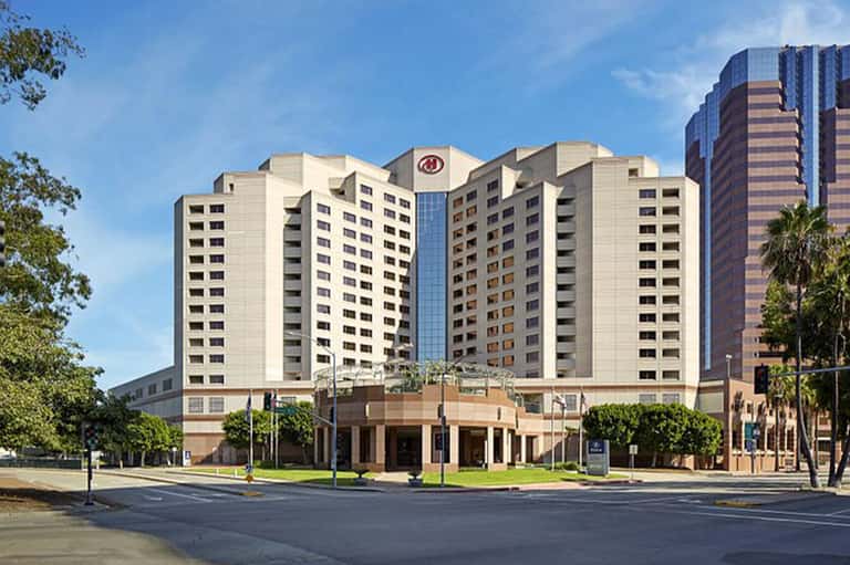 Multi-story beige hotel building with central tower and palm trees in plaza setting