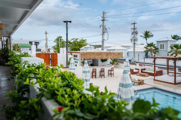 Beachfront resort pool area with striped umbrellas, lounge chairs, and thatched roof structures