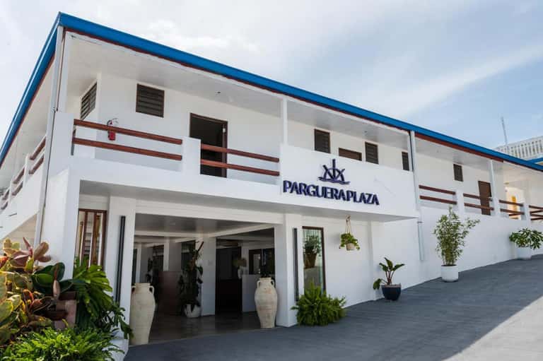 White beachfront hotel building with blue roof and red accents, palm trees entrance