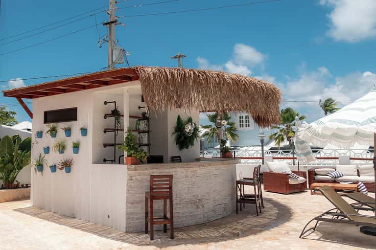Tiki bar with thatch roof, white walls, potted plants, and beach lounge area with umbrellas