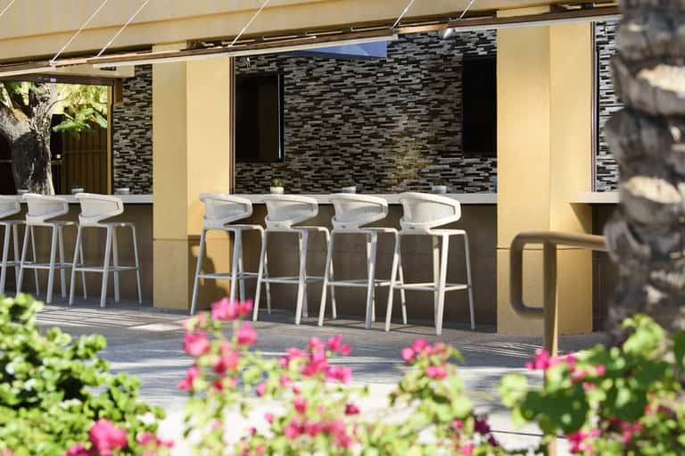 Outdoor bar with white modern stools, stucco walls, and pink flowering plants