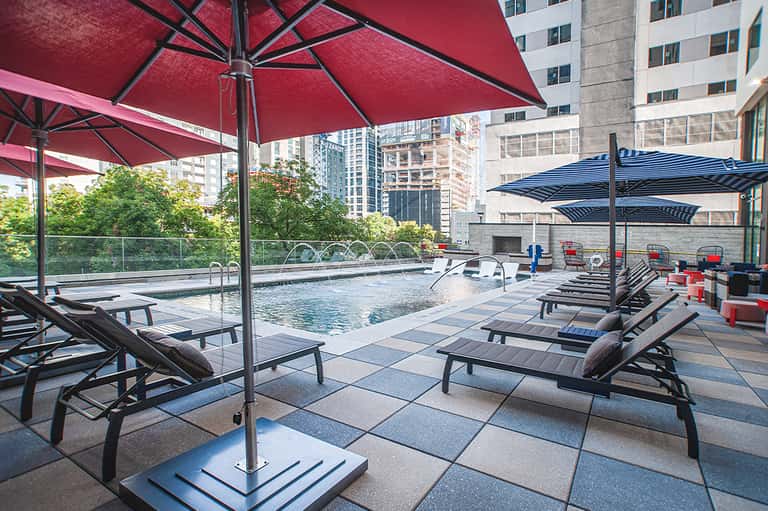 Urban rooftop pool deck with red and blue umbrellas and city skyline views