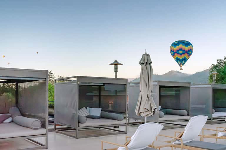 Rooftop lounge with modern cabanas, mountain views, and hot air balloons in the sky