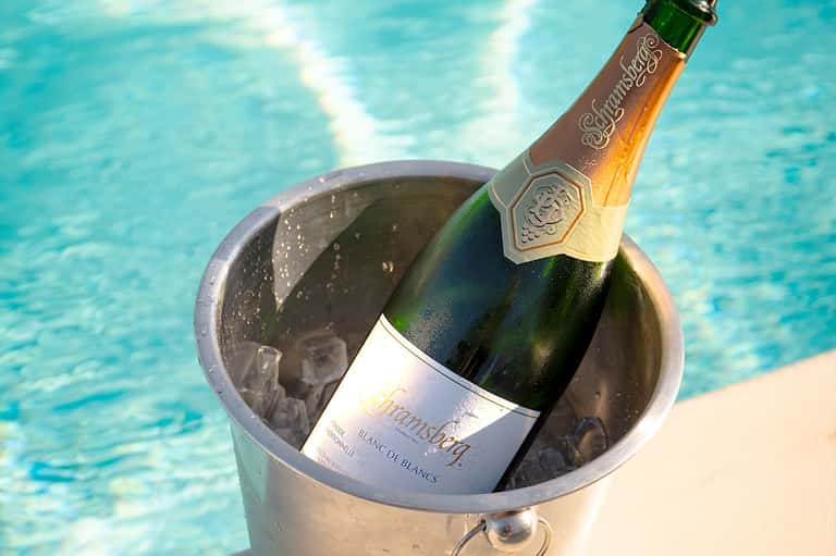Champagne bottle chilling in ice bucket poolside with turquoise water in background