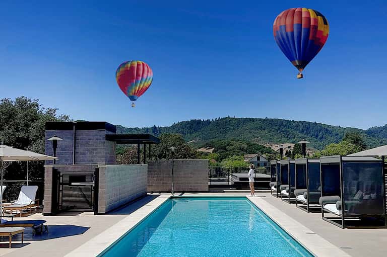 Hot air balloons floating over vineyards with rooftop pool, lounge chairs, and hillside views