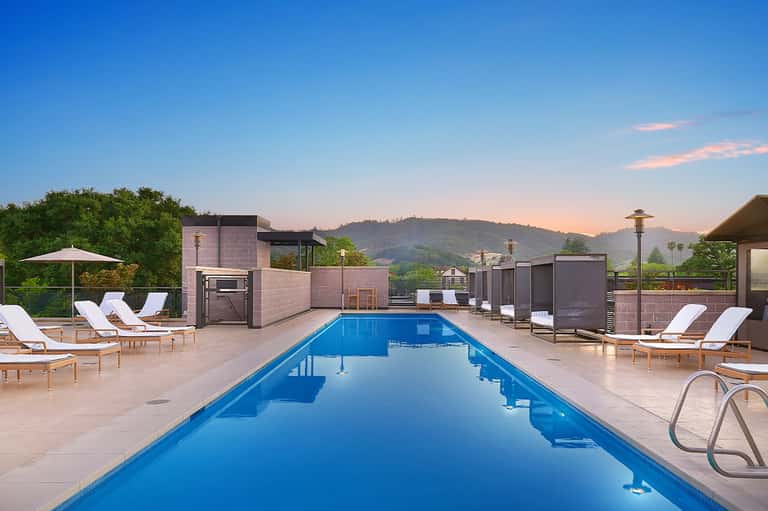 Resort infinity pool at sunset with lounge chairs, modern architecture, and mountain vista