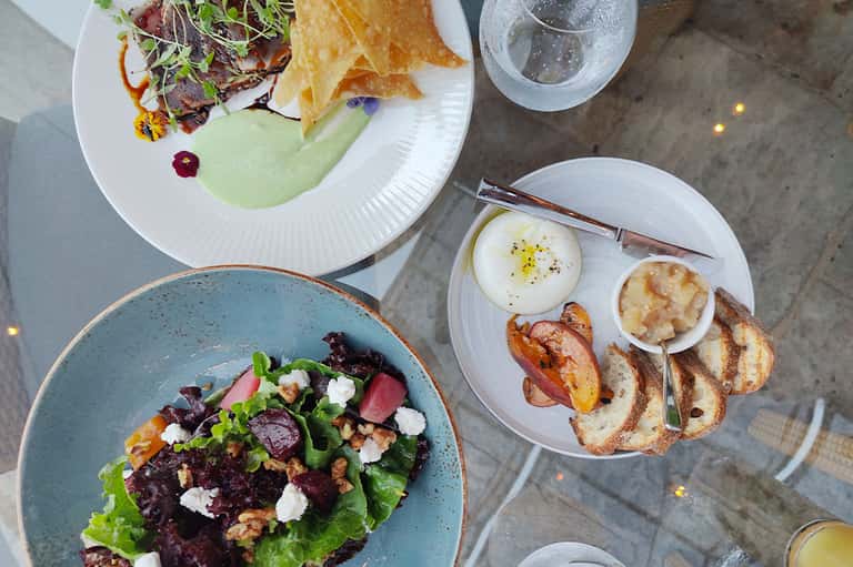 Overhead view of gourmet breakfast plates with eggs, salad, toast, and beverages