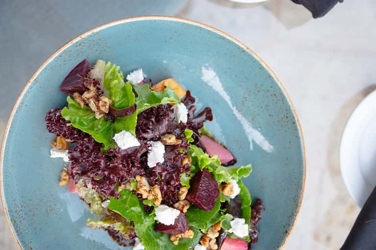 Colorful salad with beets, greens, walnuts, and goat cheese on turquoise ceramic plate