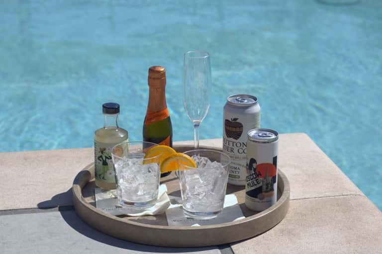 Poolside refreshment tray with bottles, champagne, glasses, and citrus garnishes on concrete deck