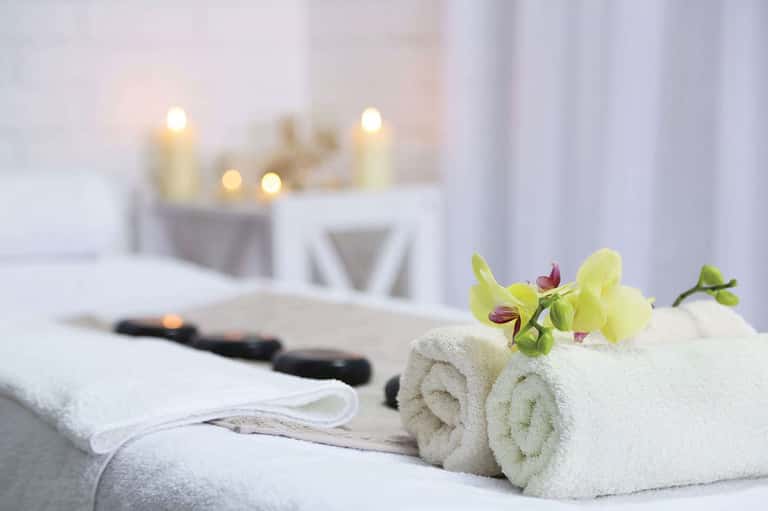 Spa treatment setup with rolled white towels, yellow orchid flowers, black stones, and lit candles