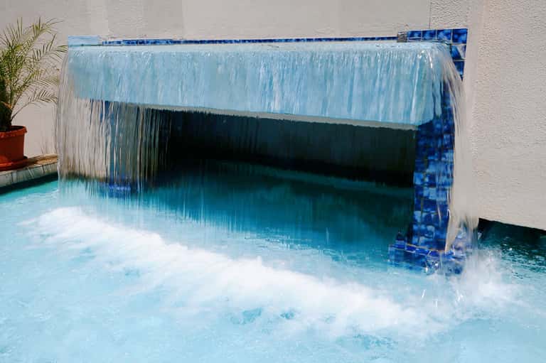 Hot spring or thermal pool with waterfall feature and blue tile surround creating white splash