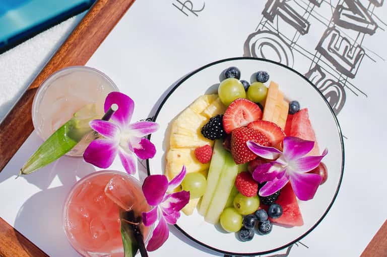 Colorful fruit platter with berries and tropical flowers, cocktail drinks on white plate with architectural sketches