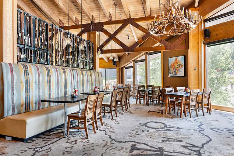 Rustic dining hall with exposed wooden beams, fireplace, and large windows overlooking nature