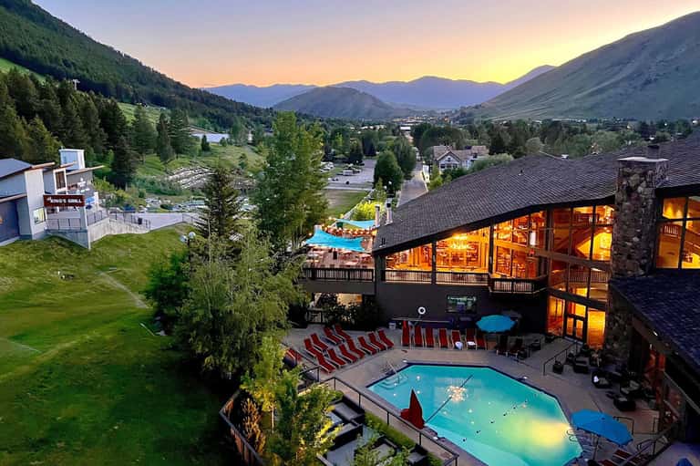 Mountain resort with lit buildings, pools, and red and white lounge chairs at sunset