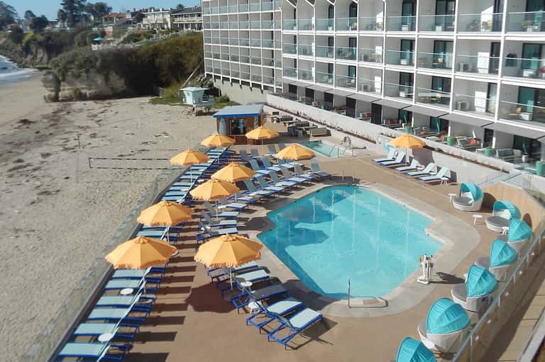 Beachfront resort pool with yellow umbrellas and loungers, sandy beach adjacent