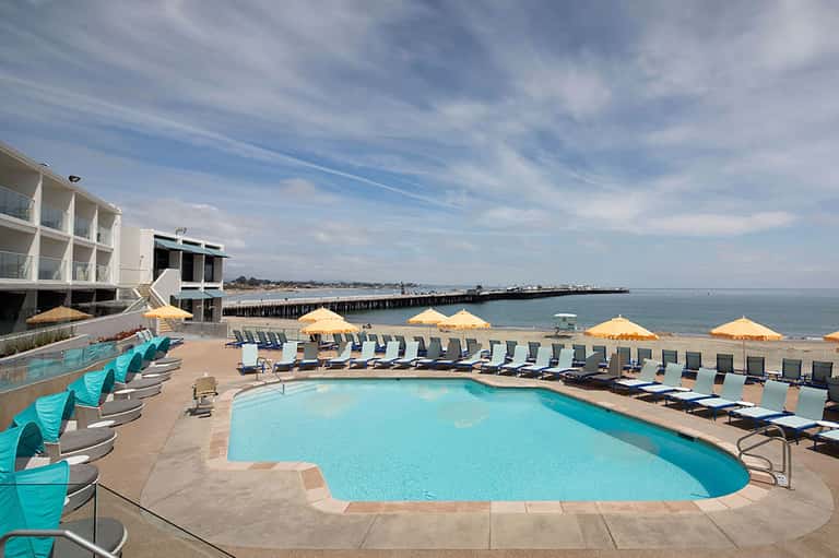 Resort pool with multiple lounge chairs and yellow umbrellas, beachfront property with pier and ocean view