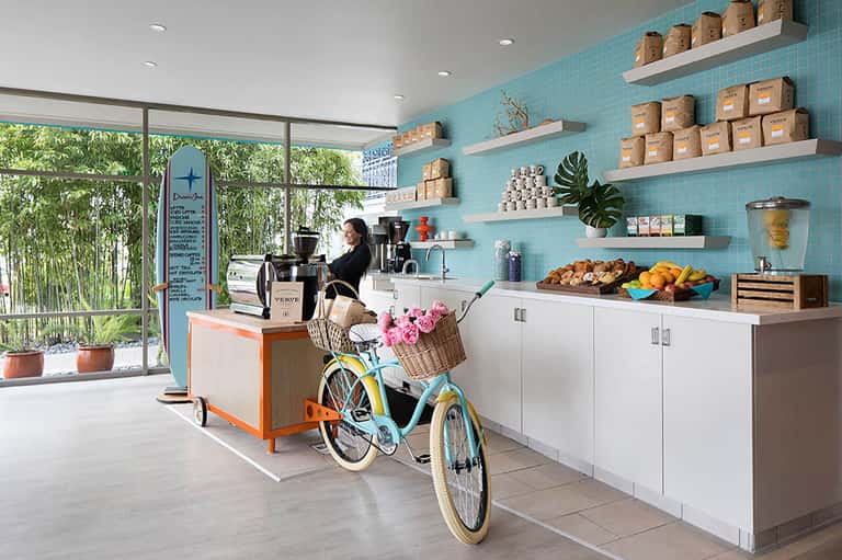 Bright turquoise cafe interior with retro bicycle, white shelving, pastries, and large windows