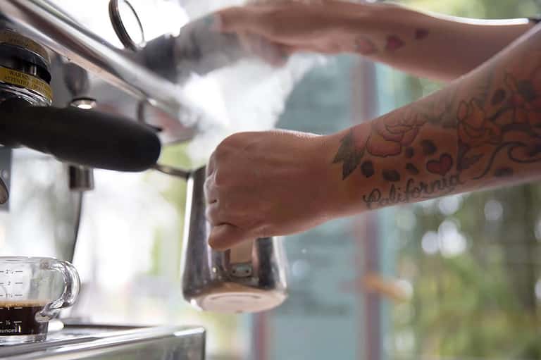 Close-up of tattooed arm pouring specialty beverage at outdoor bar counter