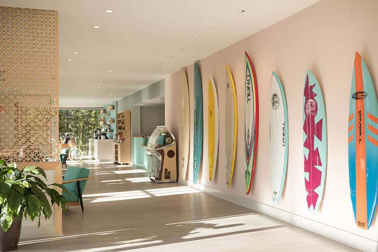 Bright hotel corridor with surfboard wall display, wooden ceiling details, and coastal decor accents
