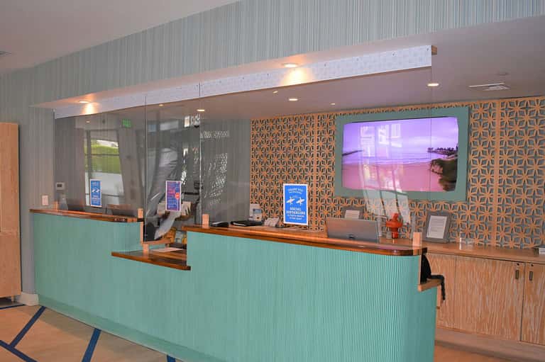 Modern hotel lobby reception desk with turquoise accents, geometric wall patterns, and digital display screen
