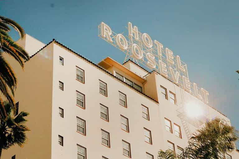 Vintage hotel building with neon sign and palm trees under clear blue sky