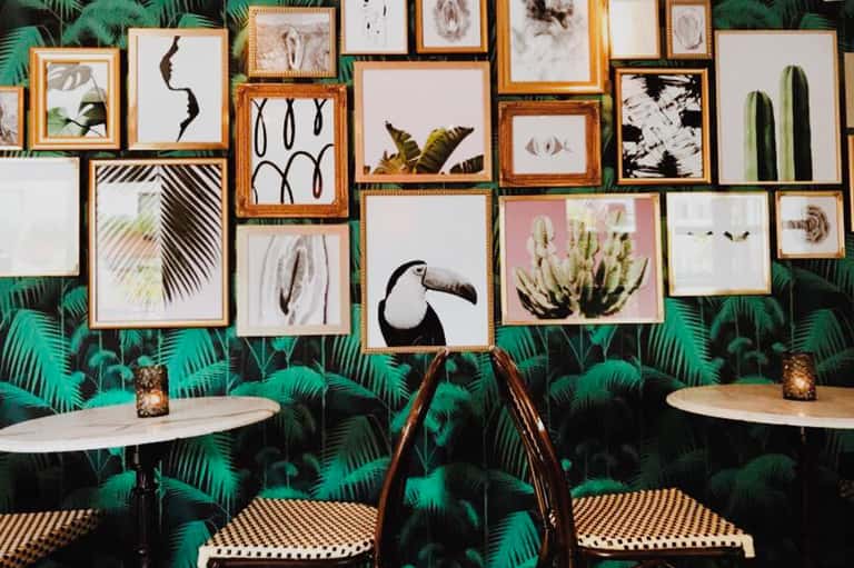 Gallery wall with framed botanical and wildlife artwork on tropical leaf wallpaper