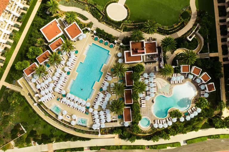 Aerial view of large resort complex with multiple pools, palm trees, and manicured grounds