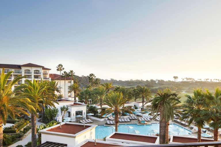Resort pool complex with palm trees, lounge chairs, and whitewashed Spanish-style building