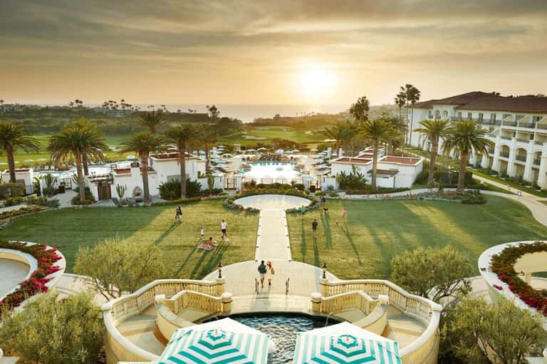 Expansive resort aerial view at sunset with pools, manicured lawns, golf course, and hotel buildings