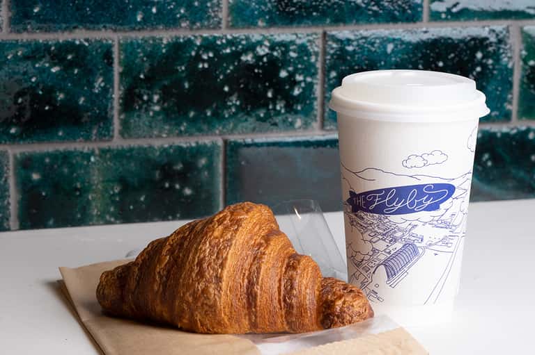 Fresh croissant and coffee cup on windowsill overlooking blue ocean tiles