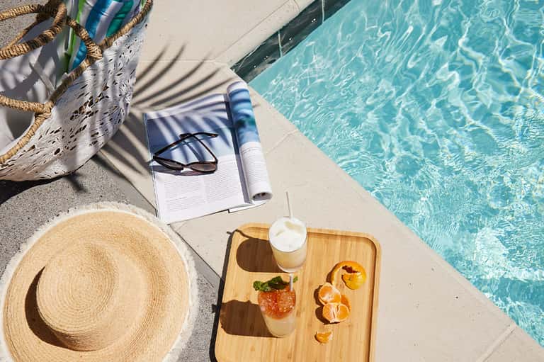 Poolside relaxation setup with straw hat, book, sunglasses, and tropical drink