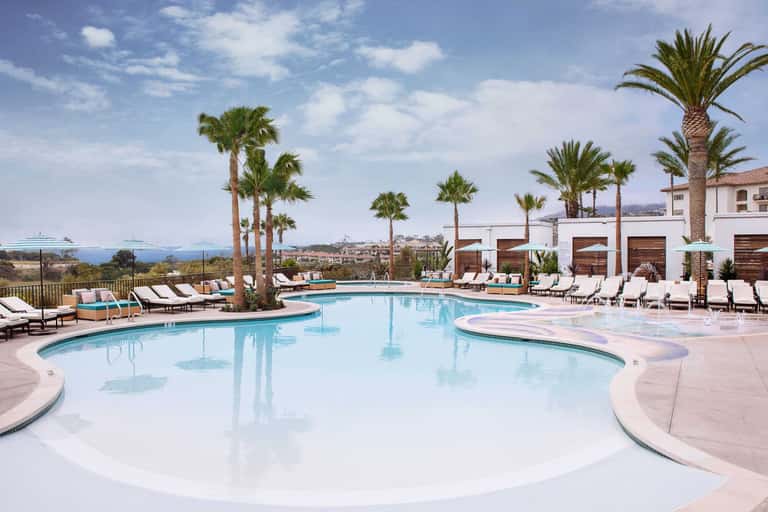 Resort pool complex with palm trees, loungers, and coastal mountain views