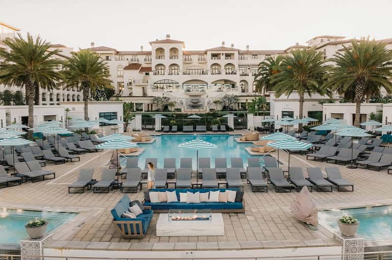 Luxury resort pool with pale blue water, loungers with umbrellas, and Mediterranean architecture