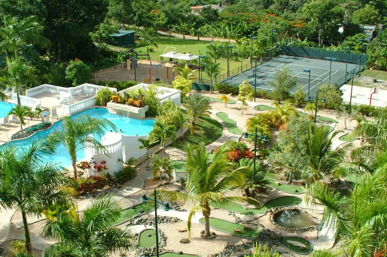 Aerial view of resort with curved pool, mini golf course, and palm trees